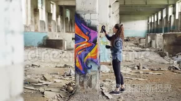 漂亮的女孩涂鸦艺术家用抽象的图片在空荡荡的工业大楼里装饰旧的损坏的柱子