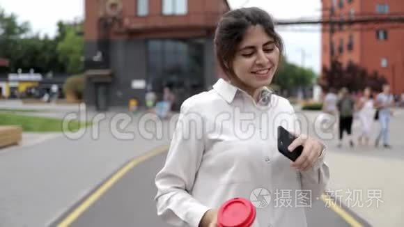 有魅力的年轻女孩带着咖啡和智能手机在街上跳舞