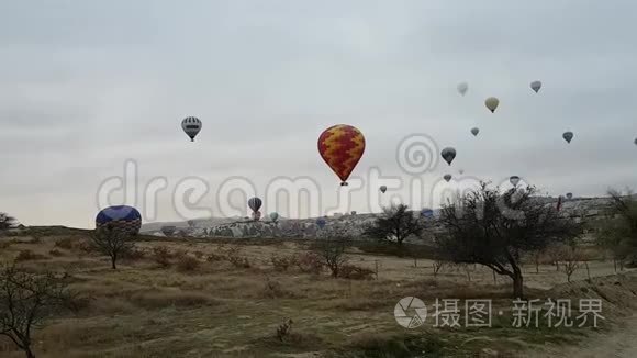 大量五颜六色的明亮气球在清晨的阴霾中飞过卡帕多西亚。 黎明和云彩笼罩戈雷姆。 慢速飞行