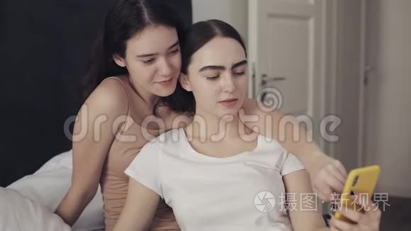 快乐的女同性恋夫妇坐在床上拥抱，用智能手机一起自拍。 女同性恋夫妇在一起
