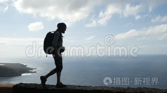 带背包的徒步旅行者正走在大洋上方加那利群岛的一条路的边缘。 特内利夫