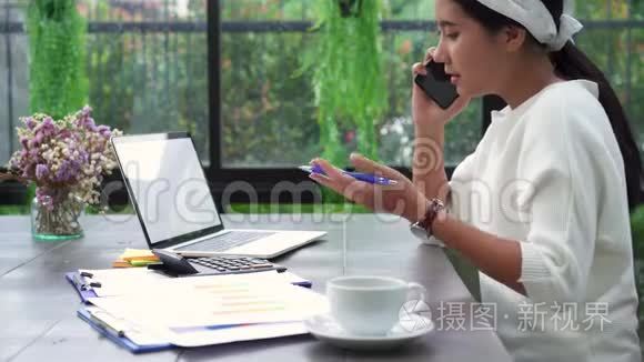 美丽的年轻压力亚洲妇女在笔记本电脑上工作，而不高兴使用智能手机在客厅在家里。