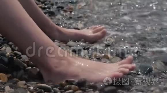 一个孩子的腿特写被波浪淹没了。 卵石沙滩喧闹的海浪拍打着孩子们双腿