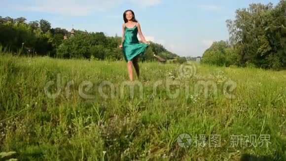 美丽微笑的年轻女子穿着绿色的裙子在草地上奔跑，在田园风光的背景下开着花