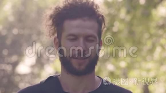 在阳光明媚的夏日公园里，一个有魅力的留胡子男子的肖像，他睁开眼睛，看着镜头，然后