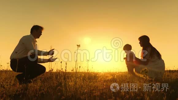 小女孩在金色的夕阳下学会用脚走路。 有爱的父母和婴儿一起走。