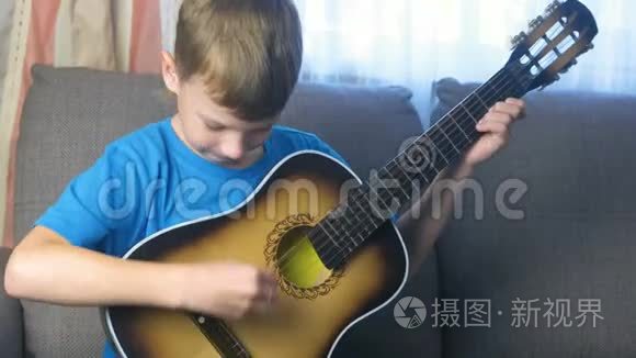 男孩学会坐在沙发上弹吉他。 学习演奏乐器的概念..
