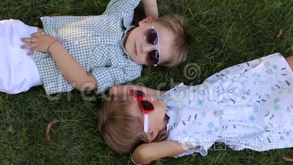 两个戴墨镜的小朋友趴在草地上头对头..