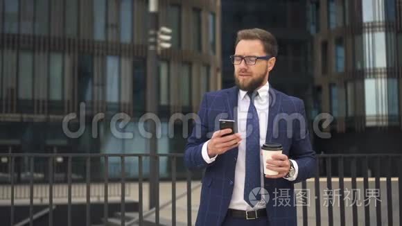 优雅的老板正在使用智能手机，拿着咖啡，站在办公楼的背景上。