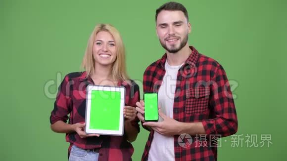 年轻夫妇一起展示数字平板电脑和智能手机