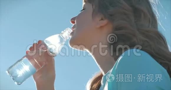 欧洲的女人出现在露天的饮料水从瓶子对抗一个晴朗的蓝天。 健康的生活方式。