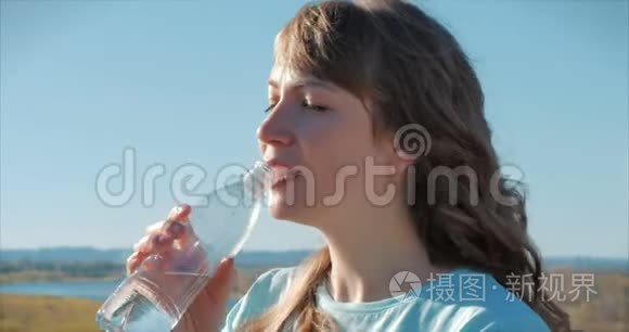 欧洲的女人出现在露天的饮料水从瓶子对抗一个晴朗的蓝天。 健康的生活方式。