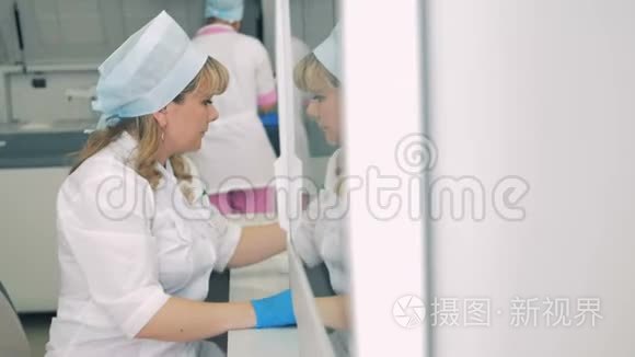 实验室里的人用设备工作。 女工人坐在桌子旁，而一个医疗离心机旋转。