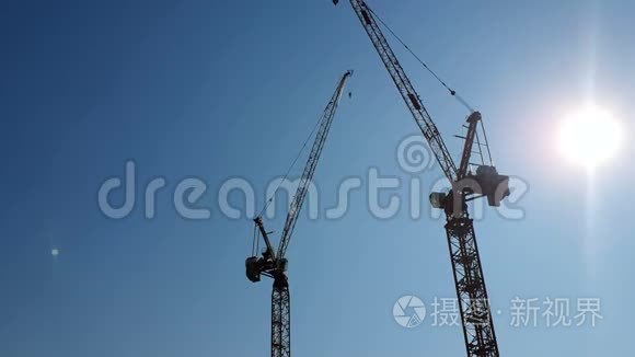 两台建筑起重机在蓝天和太阳的背景下，它在隐藏在背后的摄像机中发光