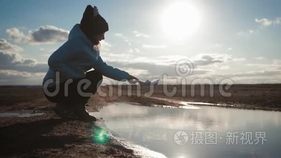 可爱的女孩在日落时在湖边玩纸船。 童梦和旅行理念，生活方式..