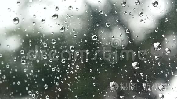 4K镜头。 雨水在透明的窗户玻璃表面，绿色的树和外面的背景。 雨滴
