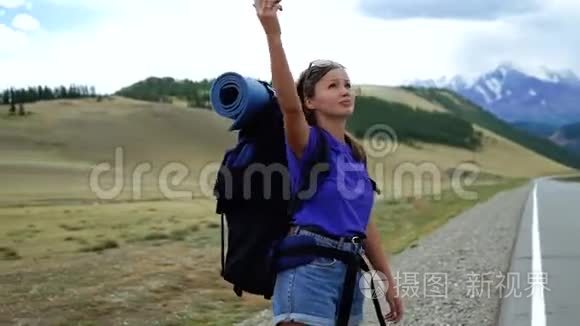 年轻的旅游妇女带着背包和太阳镜，试图在山路上捕捉电话信号。 有很多