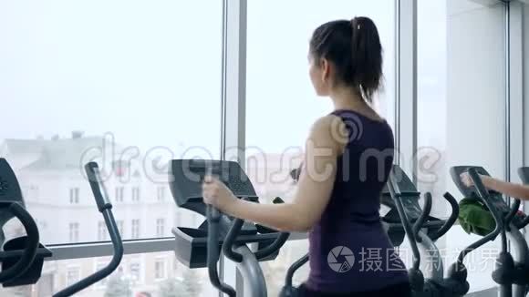 运动女孩在有大窗户的健身房运动模拟器上训练腿部肌肉