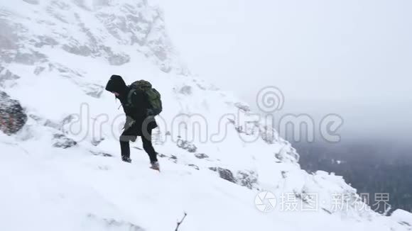 一个年轻人，一个游客，肩膀上有一个背包，上升到一座白雪覆盖的山顶。