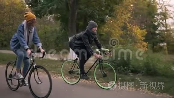 年轻的时髦夫妇骑着徒步自行车在公园里骑自行车。 两个年轻人在一起很开心
