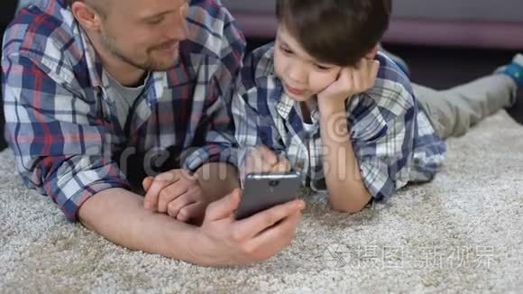 男孩和父亲在地板上玩智能手机游戏，等妈妈下班
