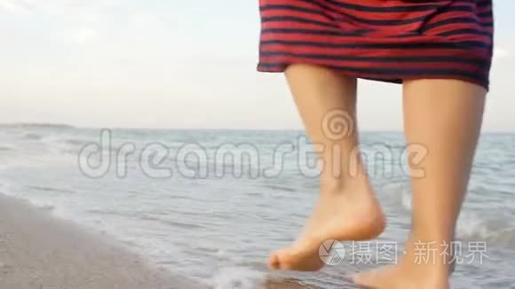 站在海边金色沙滩上的年轻女子的角度。女性的腿在海洋附近行走。赤脚的女孩继续