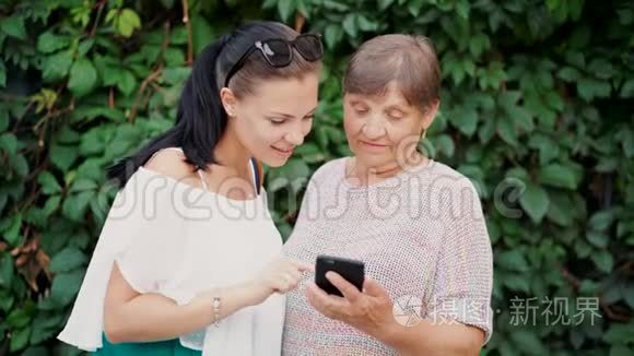 孙女在智能手机上向老奶奶展示一些东西，教她如何处理现代小工具和技术