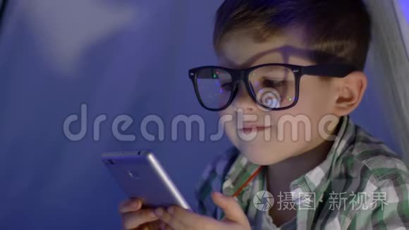 现代儿童戴眼镜的肖像，用wigwam特写镜头观看视频进入智能手机