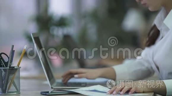 妇女从纸质文件中插入笔记本电脑数据，在办公室编写报告