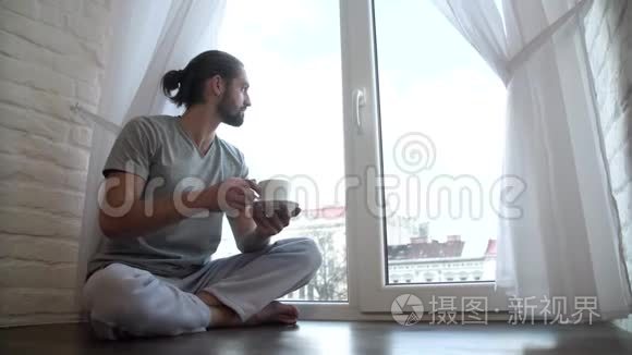 穿睡衣的男人喝咖啡坐在窗户上视频