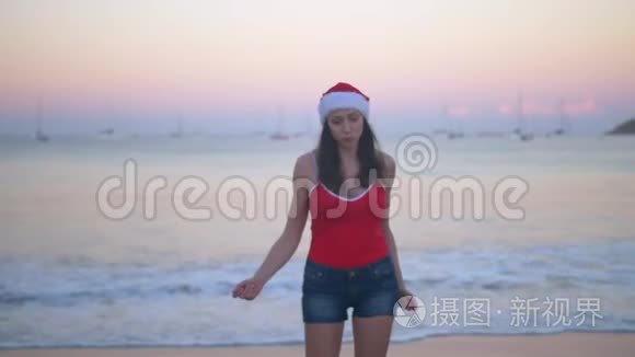 在热带天堂海滩日落时，穿着圣诞帽和红色泳衣的无忧无虑的女人跳舞和跳跃快乐