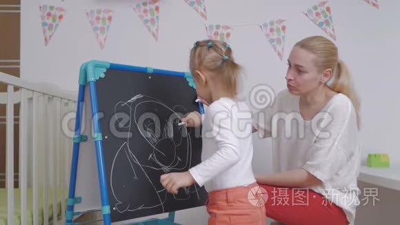 妈妈教小女孩用粉笔在黑板上画画。