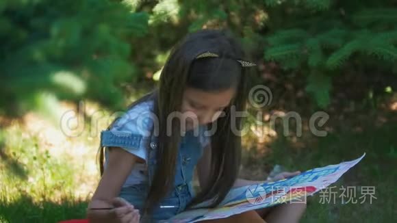 可爱的女孩画着明亮的图画，在夏天的公园里，水粉坐在草地上