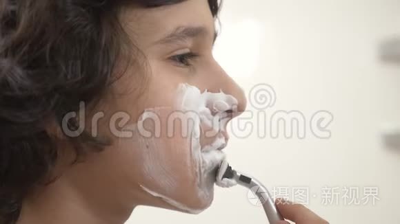青少年第一次刮胡子，十几岁的男孩用剃须泡沫，护肤品，奶油，脸，特写
