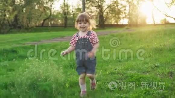 阳光明媚的夏日日落时分，快乐的小女孩在绿草上奔跑
