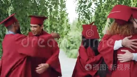 毕业的学生穿着长袍戴着帽子，兴奋的年轻人拥抱着，互相祝贺，笑着