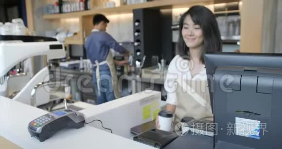 美丽的亚洲女人为一个用非接触式手机支付信用卡系统费用的顾客做外卖咖啡
