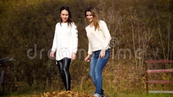 两个年轻女子将干枯的落叶踢向镜头.. 两个女孩玩黄色的秋叶。 4k60fps视频的预览图