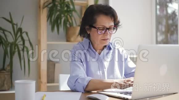 一位年长的女商人正拿着笔记本电脑坐在家里的办公室里。