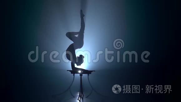 体操运动员在演播室的桌子上表演魔术。 烟雾背景。 慢动作。 剪影