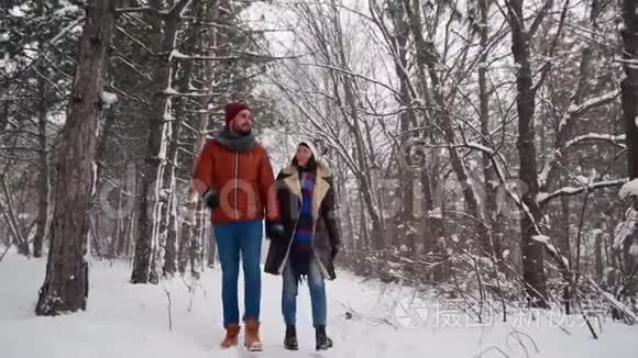 一对相爱的年轻夫妇在下雪的时候在公园里散步。男人和女友手牵手在冬日赏雪