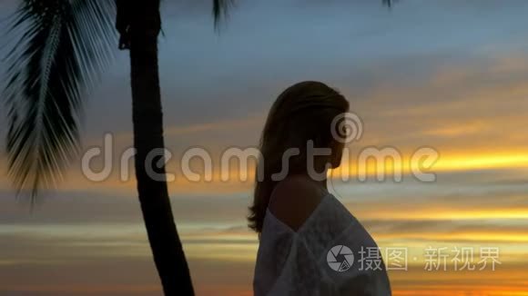 日落时分，金发女孩站在海滩上的棕榈树旁