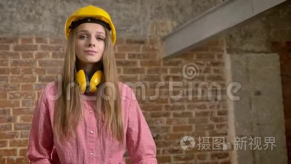 年轻自信的女建筑工人正交叉双臂，点头，看着镜头，砖背景