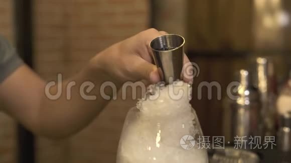 在夜总会的吧台上，酒保一边在冰上倒出蓝色的酒，一边做酒精鸡尾酒。酒保做鸡尾酒