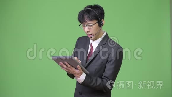 年轻快乐的亚洲商人，在呼叫中心工作时使用数字平板电脑