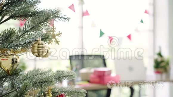 快乐的亚洲女人拿着圣诞装饰品在她的办公室装饰圣诞树。
