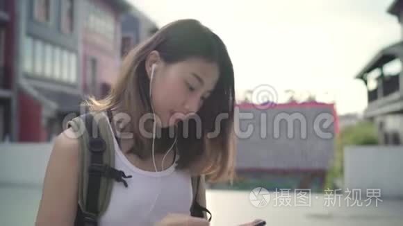 亚洲背包客博主女性使用智能手机聊天，查看社交媒体，在唐人街旅游时听音乐。