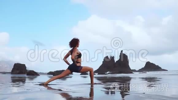 快乐的年轻女子在日落时在海滩上练习瑜伽。 健康活跃的生活方式理念.. 慢动作