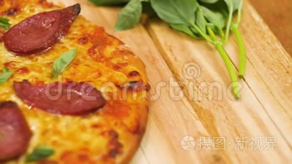 在木桌上摆着美味可口的意大利香肠比萨饼，上面装饰着绿色，没有男人或女人慢动作，靠近顶部