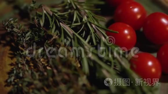 新鲜的迷迭香和美味多汁的红色西红柿躺在厨房的木板特写。 摄像机从左向右移动。
